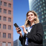 Junge Frau im Business-Outfit mit Handy in der Hand.