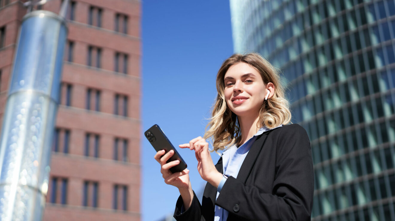 Junge Frau im Business-Outfit mit Handy in der Hand.