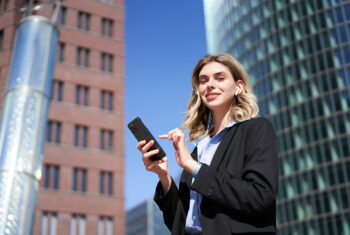 Junge Frau im Business-Outfit mit Handy in der Hand.